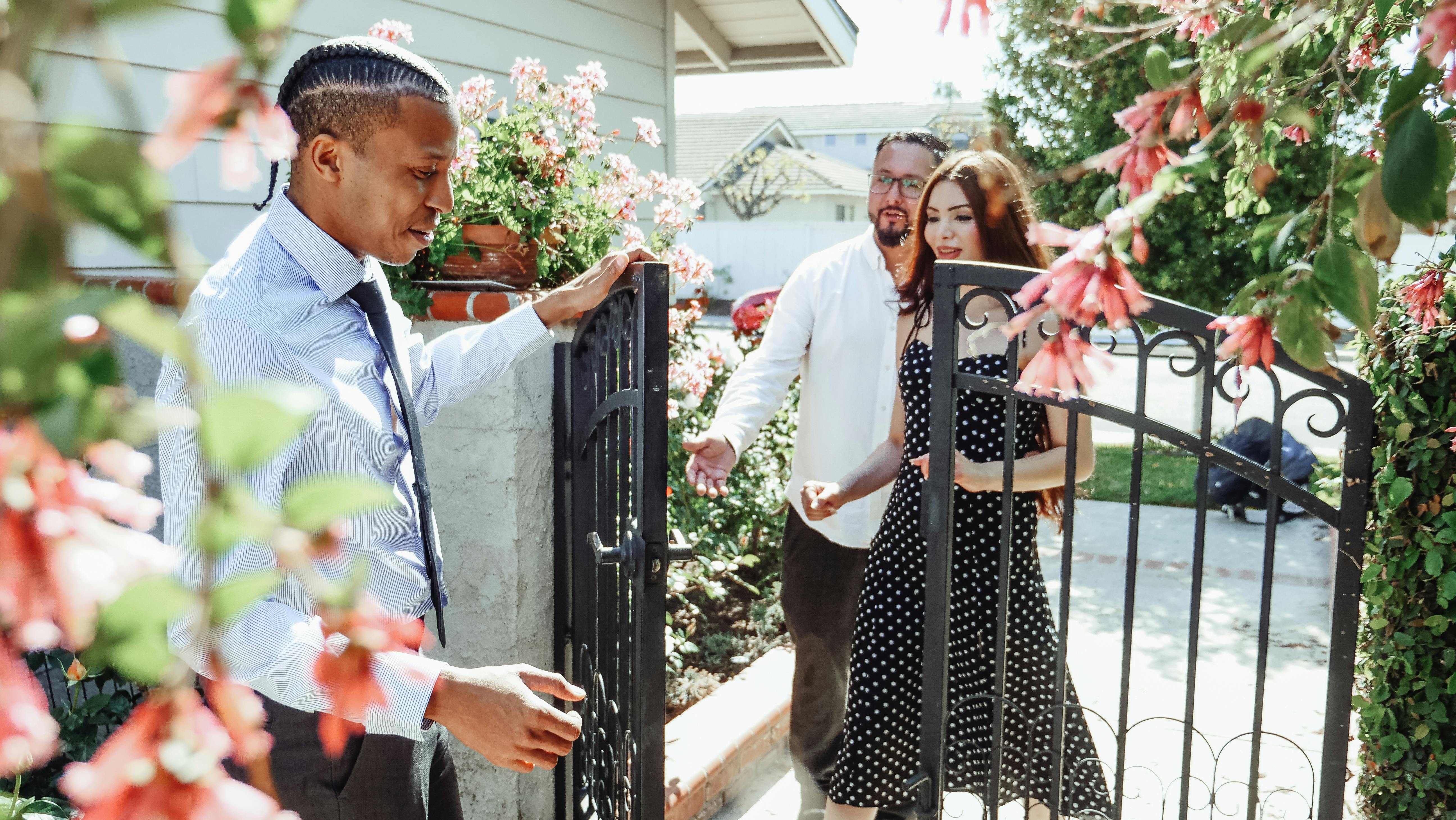 Man in Dress Shirt Holding the Gate for a Couple